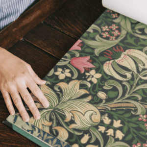 ウィリアム・モリスの代表柄「Golden Lily(ゴールデン・リリー)」の壁紙サンプルを手で広げて確認している様子。