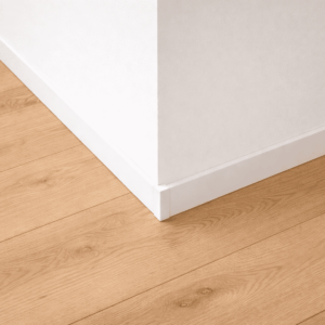 壁と床の境目に取り付けられた白い巾木をクローズアップで写した室内写真。淡い色のフローリングとシンプルな壁面の間に水平に設置された巾木が、壁面の保護部材として確認できる。