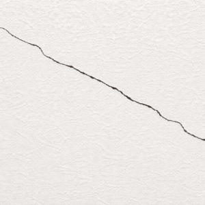 白い塗り壁の表面に細いクラックが斜めに走っている様子を写したクローズアップ写真。壁の質感とひび割れのラインがはっきり確認できる。