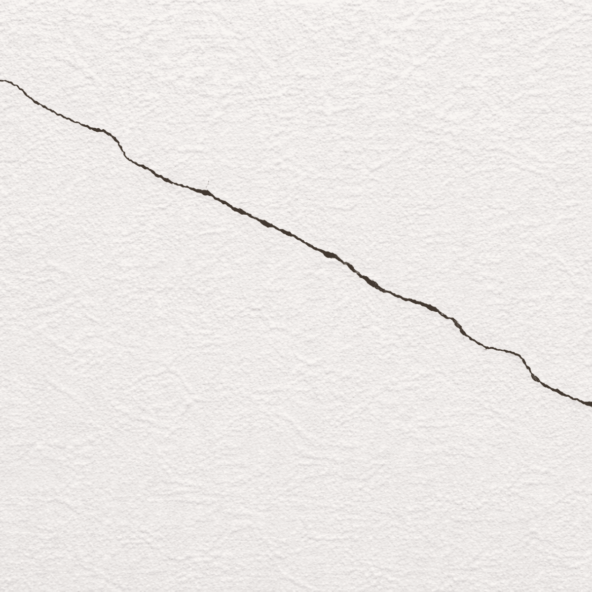 白い塗り壁の表面に細いクラックが斜めに走っている様子を写したクローズアップ写真。壁の質感とひび割れのラインがはっきり確認できる。