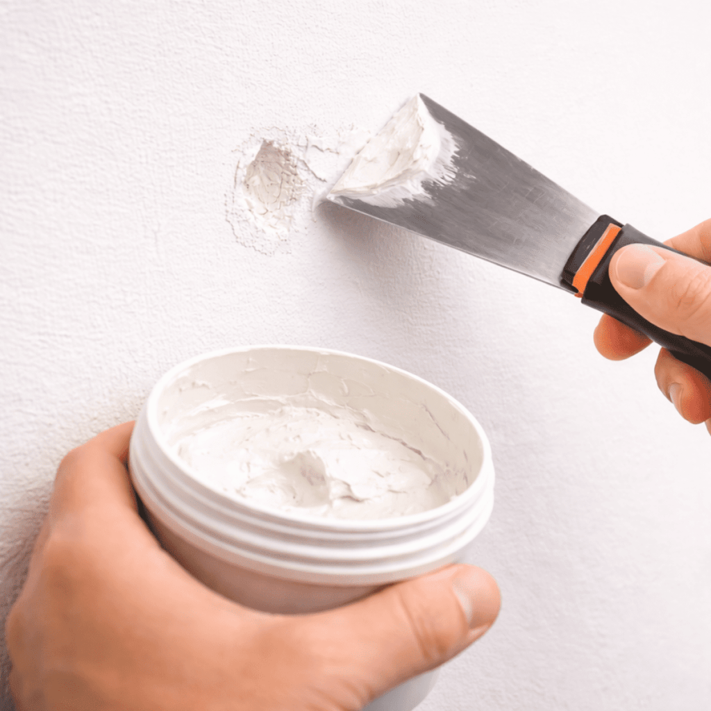 壁の小さな穴や凹み部分にパテを盛り、ヘラで表面をならして補修している様子。下地を平滑に整えるパテ埋め作業の工程がわかる接写イメージ。