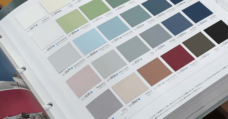 英国調の壁紙カラーサンプルブックを開いた状態。グレー、ブルー、グリーン、ベージュ、レッドなど落ち着いた色味の正方形サンプルが規則的に並び、各色に品番と名称が記載されている。