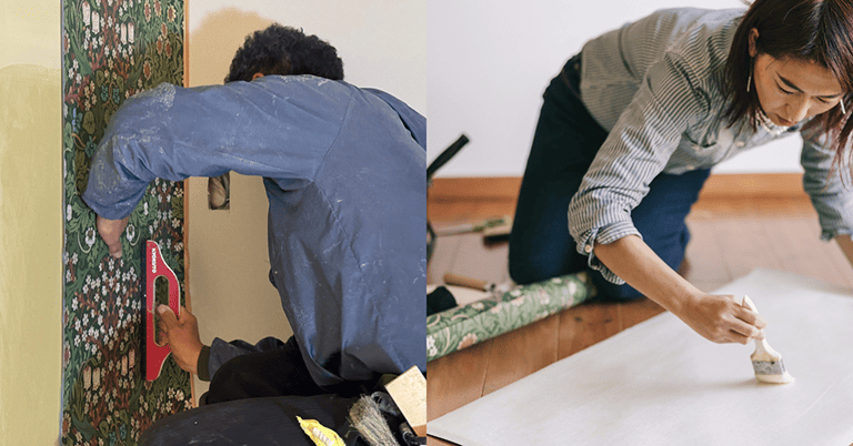壁紙施工の作業風景。左側では職人がモリス柄の壁紙を壁に当て、ヘラで位置を調整しながら貼り付けている。右側では別の作業者が床に広げた壁紙の裏面に刷毛で糊を塗っており、丁寧な手作業による施工工程が伝わる。