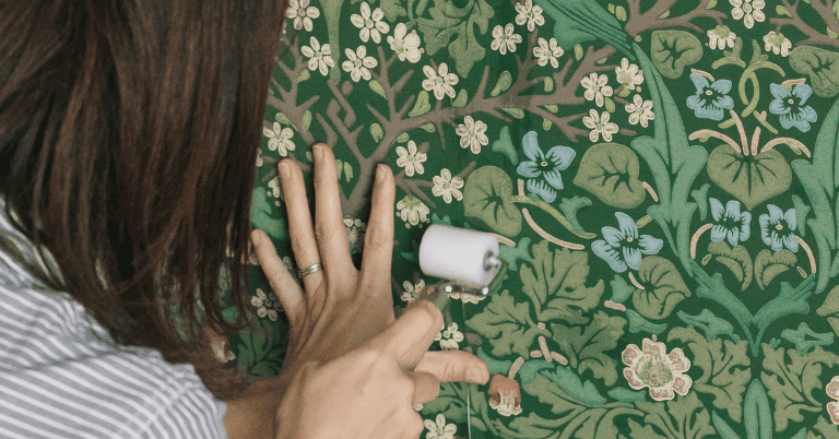 グリーンの花柄壁紙の継ぎ目をローラーで押さえて圧着しているDIY施工風景