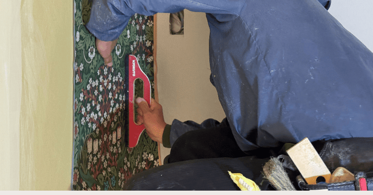 グリーンの花柄壁紙を壁に施工し、ヘラで空気を抜きながら圧着しているプロの作業風景