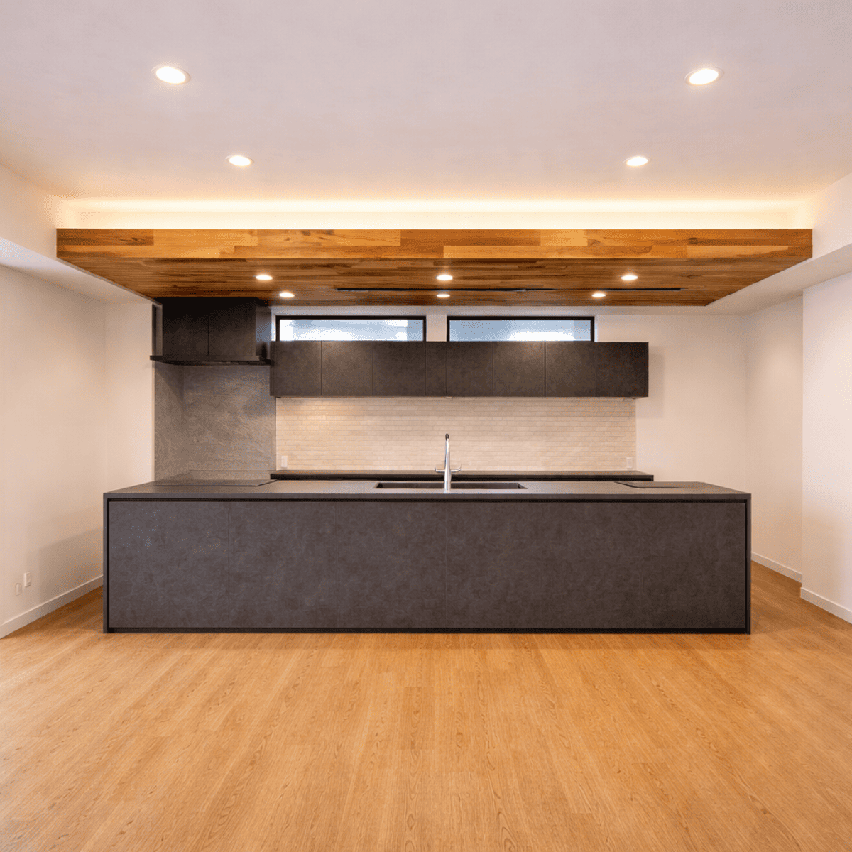 木目仕上げの下がり天井がキッチン上部に設けられた空間。間接照明とダウンライトが組み合わさり、天井の段差が奥行きと落ち着いた雰囲気を演出している室内。
