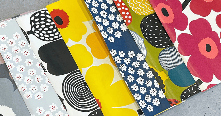 カラフルで多様なマリメッコ風の壁紙サンプルが扇状に並べられている様子。黄色や赤、青など鮮やかな配色が特徴