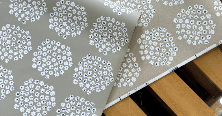 ベージュ地に白い小花が集まったマリメッコのプケッティ柄壁紙。輸入壁紙と国産壁紙の2種類が並べて広げられ、柄や色味の違いを比較している様子