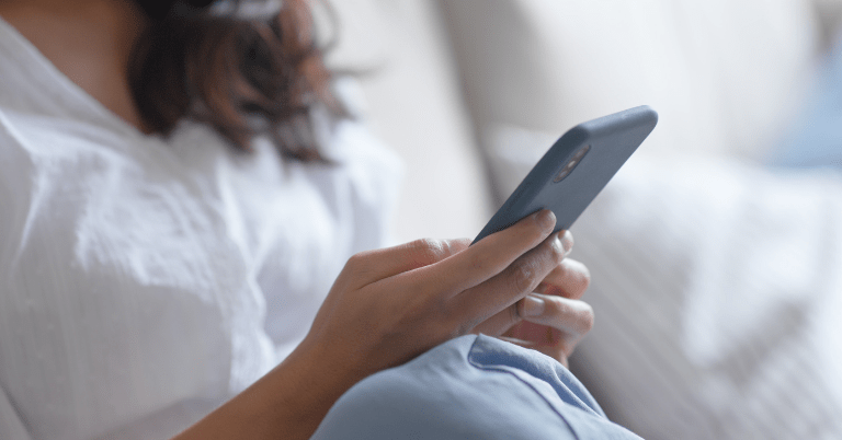 ソファに座った女性がスマートフォンを手に持ち、問い合わせや情報確認をしているイメージ