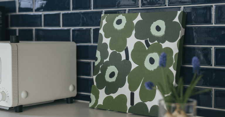 グリーンのマリメッコ・ウニッコ柄のインテリアパネルが、ネイビーのタイル壁の前に立てかけて飾られているキッチンカウンターのコーディネート