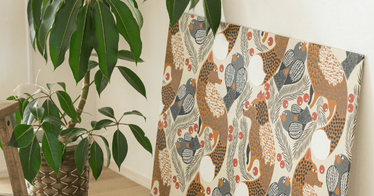 マリメッコのKetunmarja（ケトゥンマルヤ）柄のインテリアパネルが観葉植物の横に立てかけて飾られている室内コーディネート。キツネやベリー、植物モチーフの温かみのあるデザイン