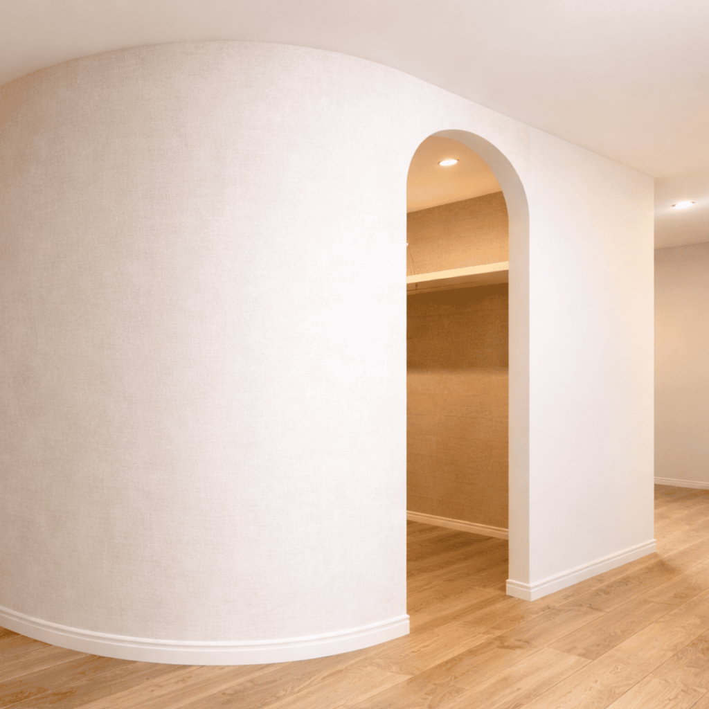 やわらかくカーブしたR壁が特徴的な室内空間。淡いベージュの壁紙と木目のフローリングが調和し、アーチ開口のデザインが印象的なインテリア。