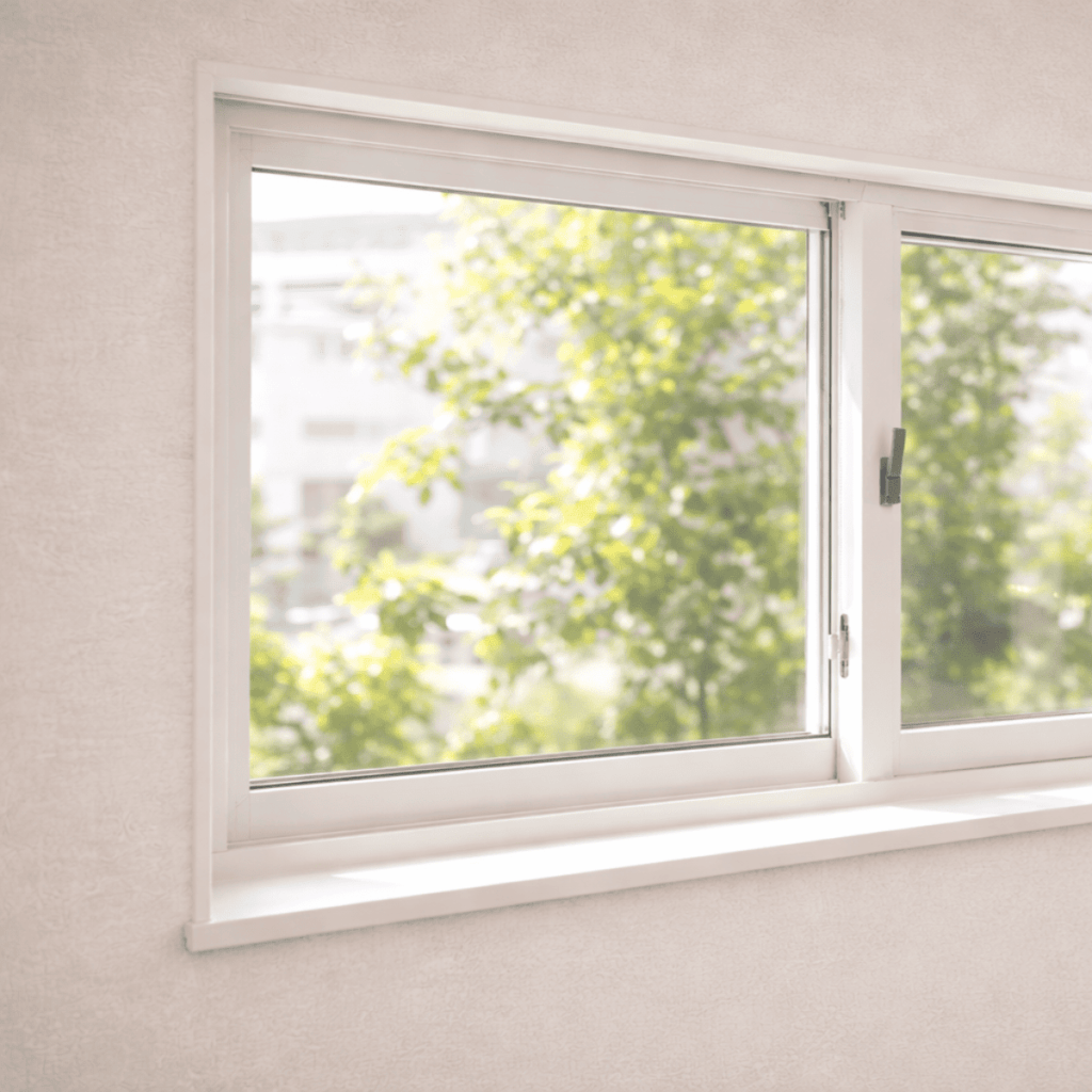 窓枠に収まった白い引き違い窓と、外の緑の景色が見える室内のシンプルな窓まわりの様子