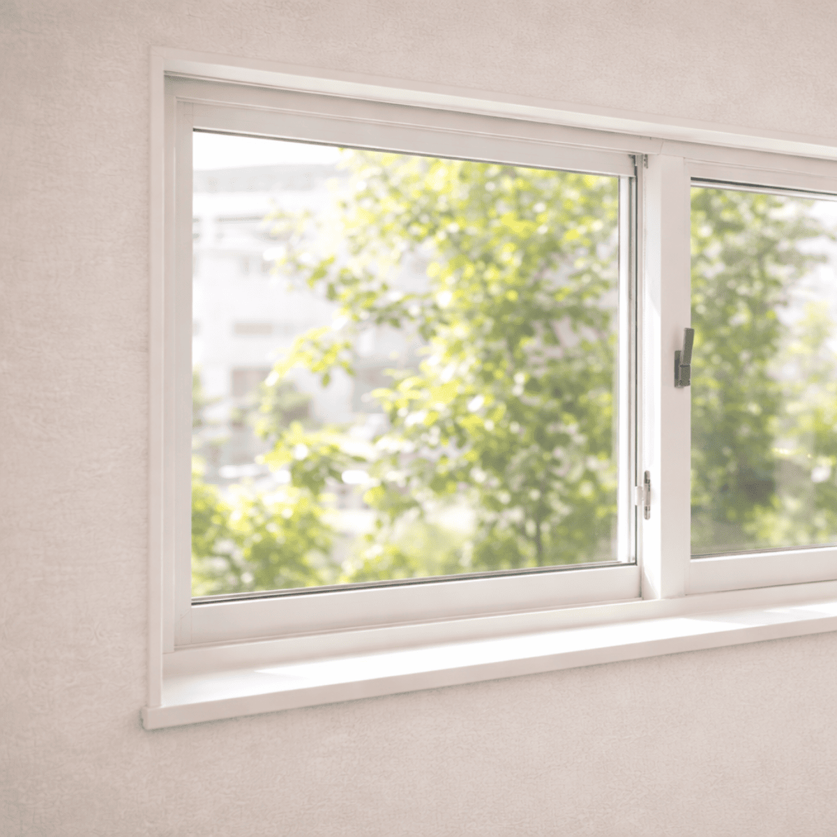 窓枠に収まった白い引き違い窓と、外の緑の景色が見える室内のシンプルな窓まわりの様子