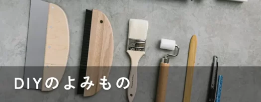 壁紙DIYに使う道具を並べた写真。スムーサー、刷毛、ローラーなどの道具が整然と並び、「DIYのよみもの」と文字が入っている。